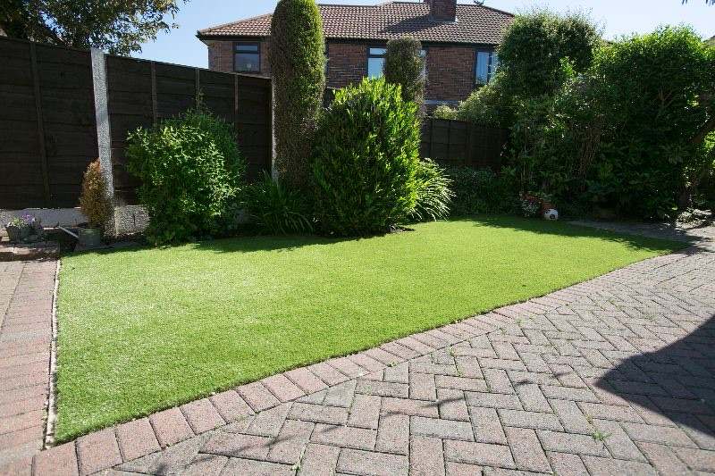 An artificial lawn beside a brick-paved driveway